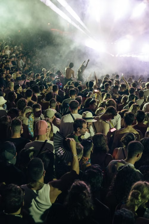 Festival crowd under smoke and bright white laser searchlights